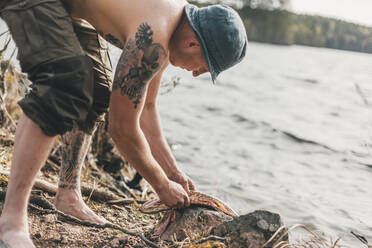 Young man gutting fish at lakeshore - GUSF03722