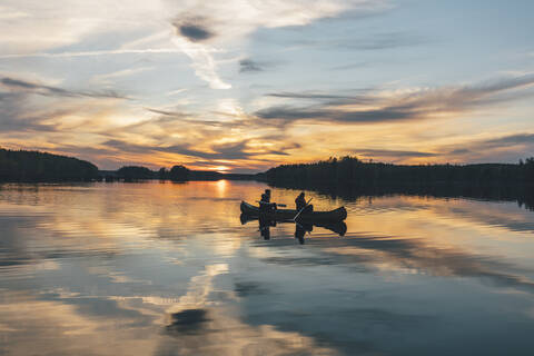 Junge Leute beim Bootfahren auf dem See bei Sonnenuntergang, lizenzfreies Stockfoto
