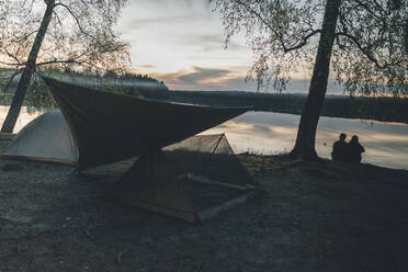 Couple camping at lake, looking at sunset - GUSF03751