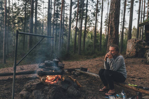 Young woman resting at camp fire, drinking tea stock photo