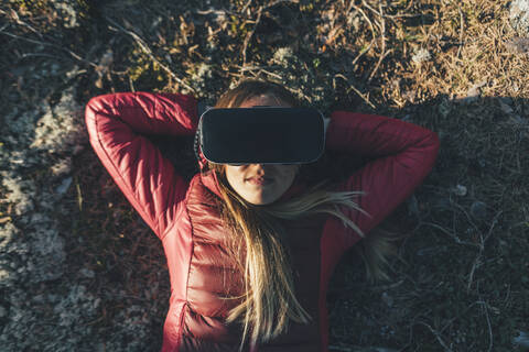 Young woman with VR goggles lying on ground in nature stock photo