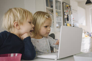 Kleines Mädchen benutzt Laptop zu Hause, während ihr älterer Bruder sie beobachtet - JOSEF00315