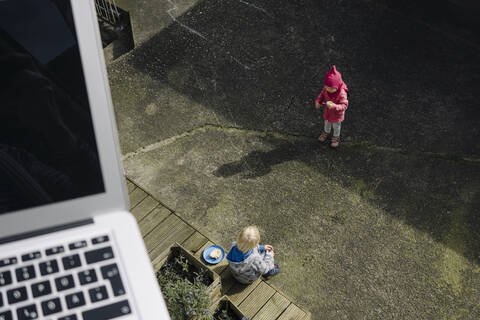 Geschwister spielen zusammen auf dem Hof mit einem Laptop im Vordergrund, lizenzfreies Stockfoto