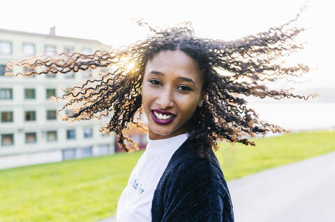 Porträt einer jungen Frau mit Locken, die ihr Haar im Gegenlicht wirft, lizenzfreies Stockfoto