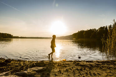 Boy walking in lake during sunset, Strausberg, Germany - OJF00388