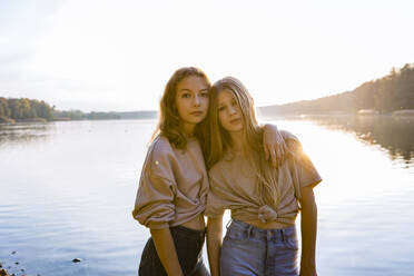 Portrait of friends standing with arm around against lake during sunset - OJF00395