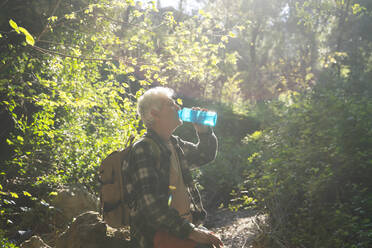 Älterer Mann mit Rucksack trinkt Wasser aus einer Flasche im Wald - AFVF06112