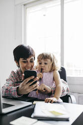 Mutter und Tochter nutzen Smartphone zu Hause - JRFF04366