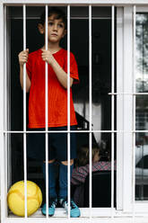 Boy with soccer ball at the window without being able to leave the house to play - JRFF04370