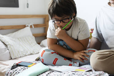 Junge liest Arbeitsbuch, während er mit seinem Vater zu Hause auf dem Bett sitzt - VABF02817