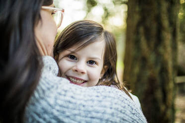 Cute young girl looking over her mothers shoulder in forest. - CAVF79472