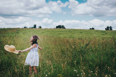 Teen Girl Twirling in einem grasbewachsenen Feld an einem bewölkten Sommertag - CAVF79534