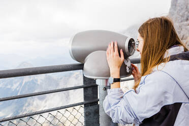 Young women looks at mountain views in binoculars from observation - CAVF79550