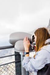 Young women looks at mountain views in binoculars from observation - CAVF79551