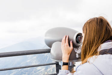 Young women looks at mountain views in binoculars from observation - CAVF79552