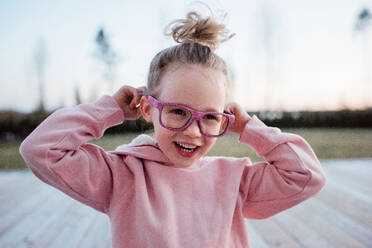 Porträt eines jungen Mädchens, das mit einer rosafarbenen, glitzernden Brille dumme Gesichter zieht - CAVF79565