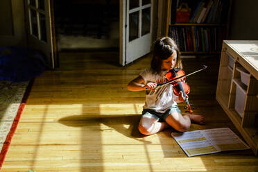 Ein kleines Kind sitzt allein auf einem sonnenbeschienenen Platz und spielt Geige - CAVF79567