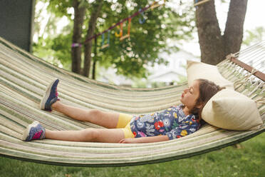 A little girl lays on a hammock by self in sunshine with closed eyes - CAVF79571