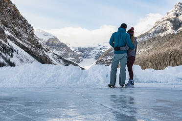 Junges Paar beim Schlittschuhlaufen auf dem Lake Louise Genießen Sie die Aussicht auf die Berge - CAVF79575