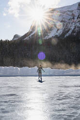 Junge Frau beim Schlittschuhlaufen auf dem gefrorenen Lake Louise an einem kalten Wintertag - CAVF79579