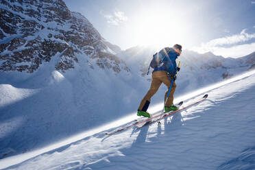 Mann beim Skitourengehen bergauf im Wind und im Gegenlicht der Sonne - CAVF79674