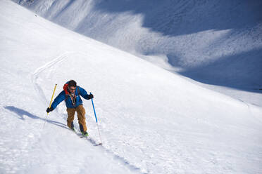 Mann in blauer Jacke beim Skitourengehen bergauf - CAVF79675