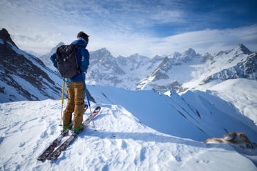 Mann auf Skiern auf einem Bergrücken mit Blick auf die Berge - CAVF79677