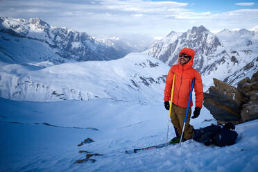 Skifahrer in orangefarbener Jacke, der sich auf die Stöcke stützt und lacht - CAVF79678