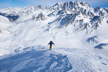 Man ski touring up slow with mountain behind him - CAVF79685