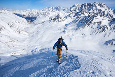 Mann beim Skitourengehen auf der Piste mit den Bergen hinter ihm - CAVF79686