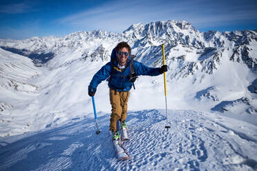 Smiling man ski touring up slope with mountains behind - CAVF79688