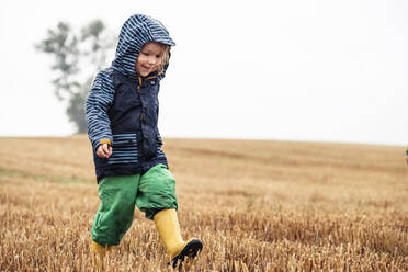 Glückliches kleines Mädchen, das auf einem Stoppelfeld an einem regnerischen Tag spazieren geht - WFF00372