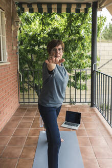 Ältere Frau praktiziert Yoga mit Laptop auf dem Balkon - XLGF00065