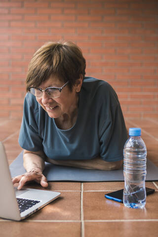 Ältere Frau benutzt Laptop auf Balkon, lizenzfreies Stockfoto