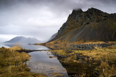 Island, Wolken über ruhigem Seeufer mit Bergen im Hintergrund - DAMF00418