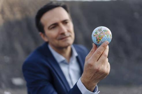 Älterer Geschäftsmann hält einen Globus auf einer stillgelegten Minenhalde - JOSEF00352