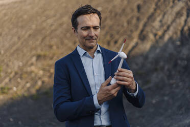 Mature businessman on a disused mine tip holding wind turbine model - JOSEF00437