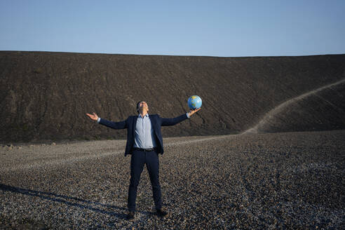 Mature businessman holding a globe on a disused mine tip - JOSEF00466