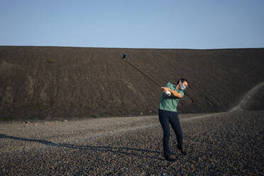 Älterer Mann mit Maske spielt Golf auf einer stillgelegten Minenhalde - JOSEF00468