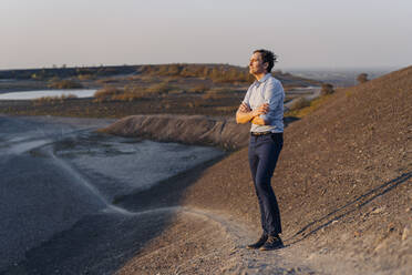 Mature businessman standing on a disused mine tip looking at view - JOSEF00484