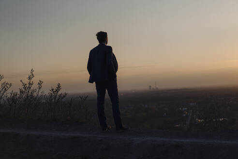 Mature businessman standing on a disused mine tip at sunset looking at view - JOSEF00495