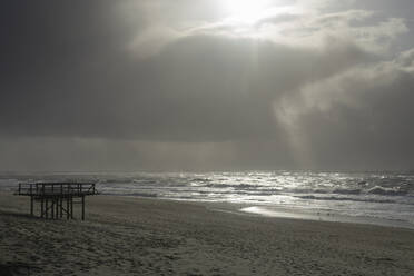 Germany, Schleswig-Holstein, Westerland, Sunlight piercing through storm clouds over coastal beach of North Sea - WIF04253