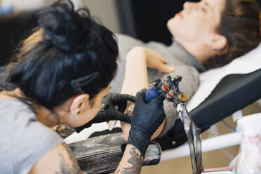 Female tattooist tattooing on a woman's arm - JSMF01540