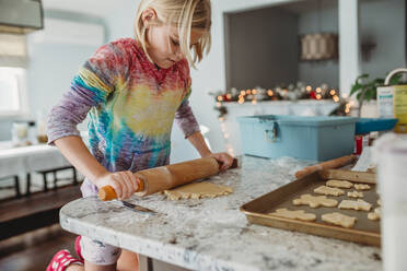 Girl Rolling out dough with Christmas lights in the background - CAVF79852