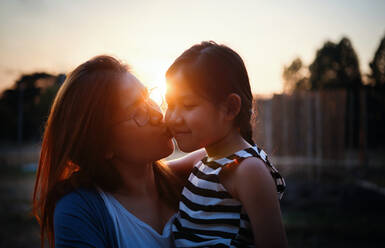 Mother kissing her daughter during sunset - CAVF79897