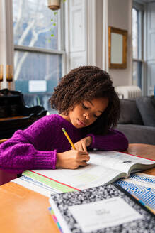 Girl doing homework while sitting at table in living room - CAVF79900