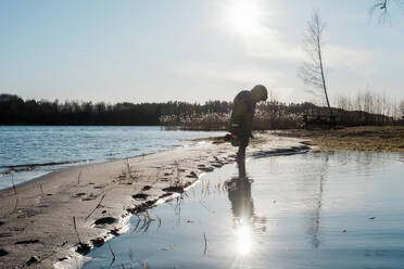 Kleiner Junge spielt im Wasser am sonnigen Strand im Winter - CAVF79944