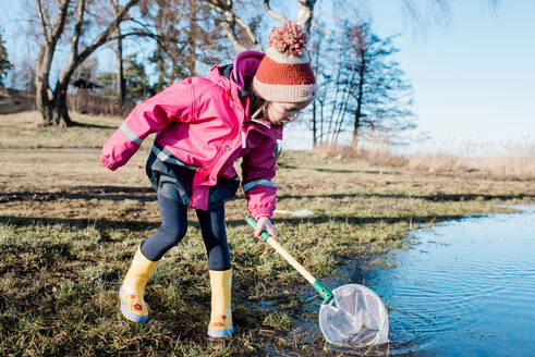 Junges Mädchen spielt mit einem Fischernetz im Meer an einem sonnigen Wintertag - CAVF79946