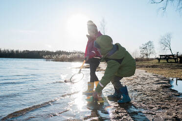 Brother and sister playing with nets and toys at a sunny beach - CAVF79947