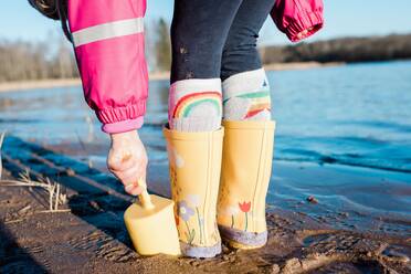 Regenstiefel und Spaten eines kleinen Kindes am Strand in der Sonne - CAVF79949